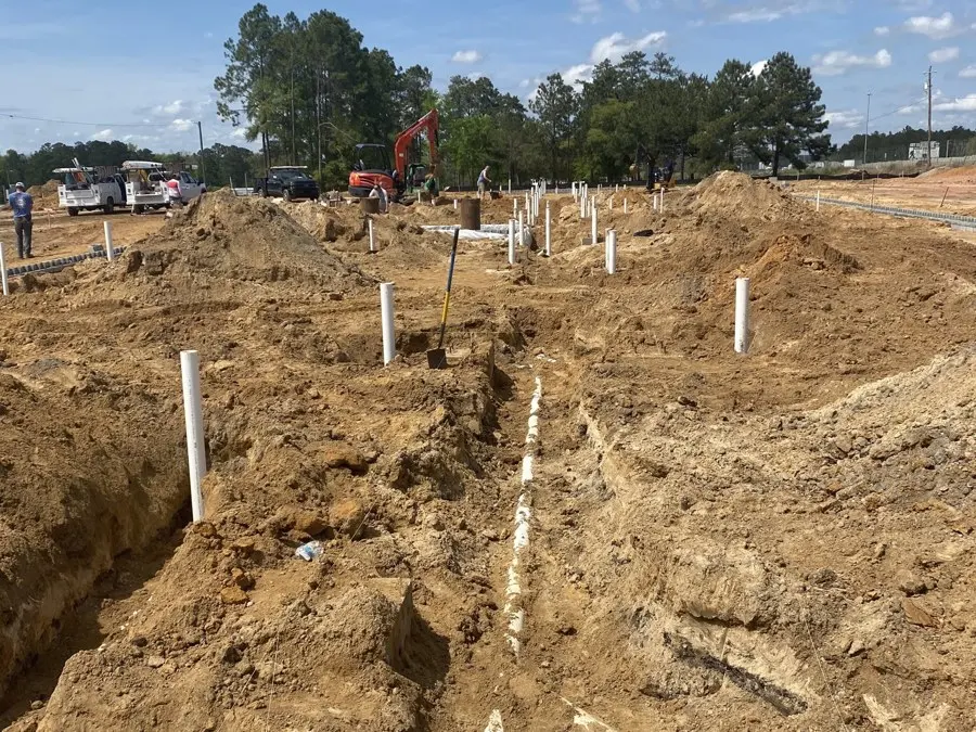 Open trench in red clay with white PVC pipe